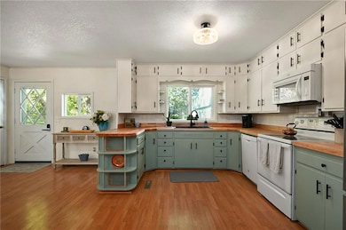 Kitchen featuring green cabinetry, open shelves, white appliances, butcher block counters, and a textured ceiling