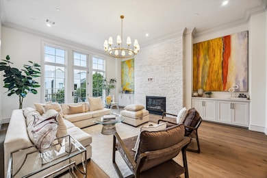 The lavish living room, complete with custom built-ins, stacked stone fireplace, and floor-to-ceiling windows. Twelve-foot ceilings, elegant crown moulding, and understated chandelier by Ziba create warmth and elegance.