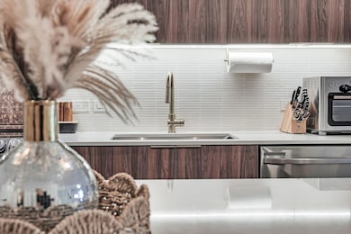 Kitchen with modern cabinets, dishwasher, dark brown cabinets, backsplash, and light countertops