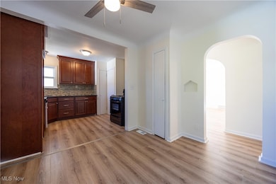 Kitchen with black range with gas stovetop, light wood-style flooring, tasteful backsplash, arched walkways, and ceiling fan