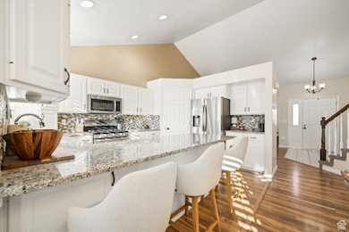 Kitchen with tasteful backsplash, light stone counters, dark wood-type flooring, lofted ceiling, and a kitchen breakfast bar
