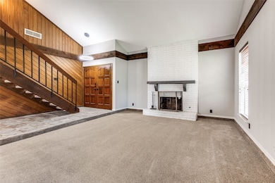 Unfurnished living room with wood walls, stairs, carpet flooring, a brick fireplace, and high vaulted ceiling