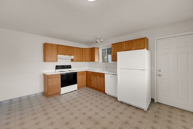 Kitchen with white appliances, light countertops, light flooring, brown cabinets, and under cabinet range hood