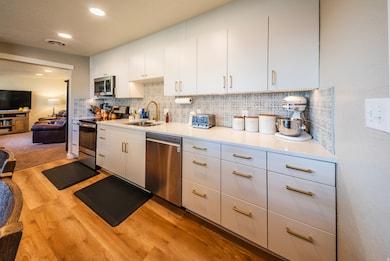 Kitchen with stainless steel appliances, white cabinets, decorative backsplash, light wood-style flooring, and recessed lighting