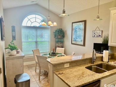 Kitchen featuring a sink, lofted ceiling, pendant lighting, light tile patterned floors, and white cabinets