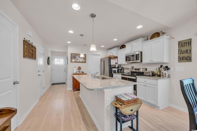 Kitchen with appliances with stainless steel finishes, a sink, light wood-type flooring, white cabinets, and recessed lighting