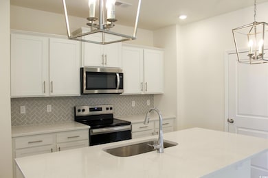Kitchen with a chandelier, backsplash, stainless steel appliances, white cabinetry, and light stone counters