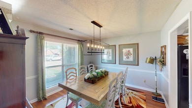 Dining area with a chandelier, wood finished floors, a textured ceiling, and baseboards