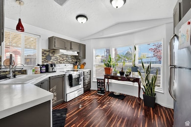 Kitchen with freestanding refrigerator, light countertops, vaulted ceiling, electric stove, and gray cabinetry