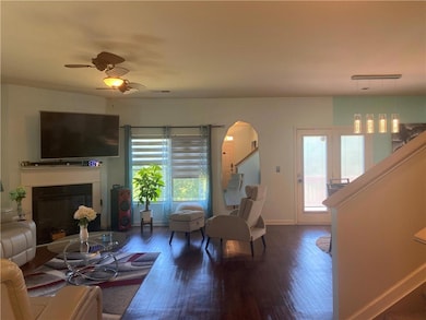 Living room featuring wood finished floors, a fireplace, arched walkways, ceiling fan, and stairway