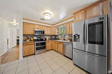 Kitchen featuring appliances with stainless steel finishes, tasteful backsplash, light tile patterned floors, open shelves, and light brown cabinets