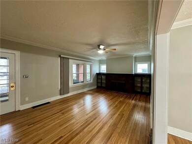 Unfurnished living room with a textured ceiling, visible vents, ornamental molding, ceiling fan, and hardwood / wood-style floors