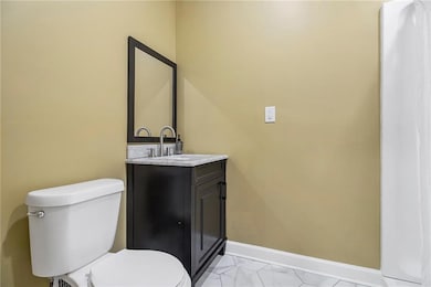 Bathroom with toilet, marble look tile flooring, vanity, and baseboards