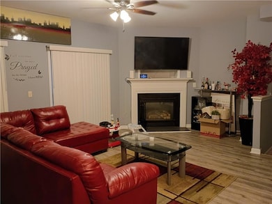 Living area featuring a glass covered fireplace, light wood finished floors, and a ceiling fan