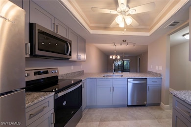 Kitchen featuring stainless steel appliances, gray cabinets, a tray ceiling, light stone counters, and ornamental molding