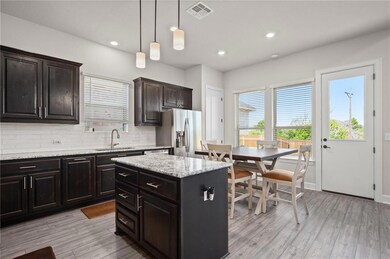 Kitchen featuring light stone countertops, dark brown cabinetry, backsplash, stainless steel refrigerator with ice dispenser, and hanging light fixtures