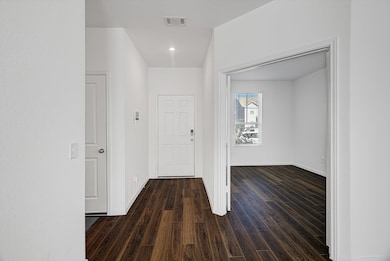 This photo showcases a bright entryway with dark wood flooring, leading to a room on the right with a large window, allowing natural light to enhance the space.
