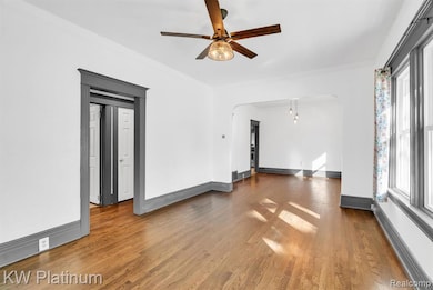 Empty room featuring wood finished floors, baseboard heating, arched walkways, and ceiling fan