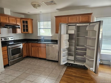 Kitchen with appliances with stainless steel finishes, glass insert cabinets, brown cabinets, under cabinet range hood, and light tile patterned floors