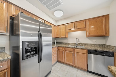 Kitchen with appliances with stainless steel finishes, dark stone countertops, light tile patterned floors, and brown cabinets