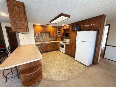 Kitchen with open shelves, white appliances, light countertops, a kitchen bar, and a textured ceiling