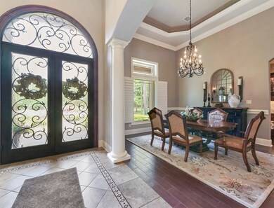 The grand foyer offers gorgeous ornamental iron & glass doors & formal dining to the left. Notice the lovely wood & tile floors, trey ceiling, shutters & columns