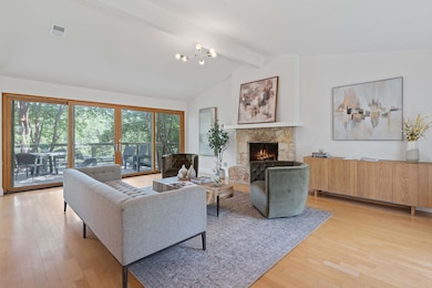 Living area featuring a stone fireplace, light wood-style flooring, and a chandelier
