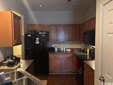 Kitchen with black appliances, dark wood-type flooring, brown cabinetry, and dark countertops