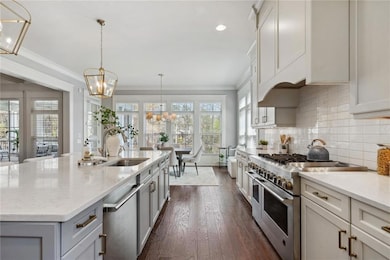 Kitchen with light countertops, an island with sink, built in fridge, backsplash, and a notable chandelier
