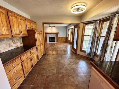 Kitchen with dark countertops, a textured ceiling, brown cabinets, a fireplace, and white dishwasher