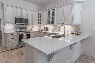Kitchen with stainless steel appliances, glass insert cabinets, a breakfast bar area, a peninsula, and light stone countertops