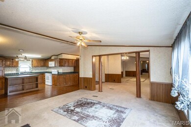 Family room with light carpet, a textured ceiling, lofted ceiling, ceiling fan, large window, and partial wooden walls. Open to kitchen and to dining room.