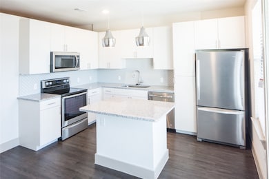 Kitchen with white cabinets, hanging light fixtures, sink, and appliances with stainless steel finishes
