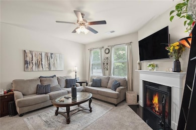 Living area with carpet floors, ceiling fan, and a fireplace with flush hearth