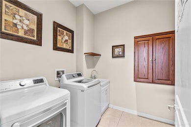 Clothes washing area with cabinets, sink, washer and dryer, and light tile patterned floors