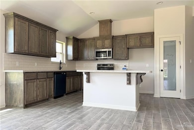 Kitchen with vaulted ceiling, stainless steel appliances, tasteful backsplash, light wood-type flooring, and a kitchen island