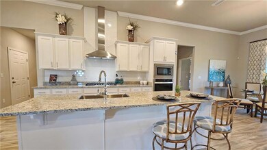 Kitchen with light wood-type flooring, wall chimney range hood, a breakfast bar area, white cabinets, and ornamental molding
