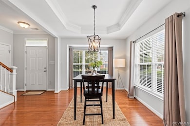 Dining space with a chandelier, a tray ceiling, ornamental molding, and light hardwood flooring