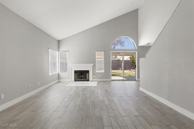 Unfurnished living room featuring high vaulted ceiling, a fireplace with flush hearth, and wood finish floors