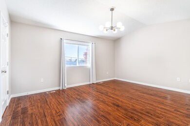 Large primary bedroom with dark wood-type flooring, a chandelier, and vaulted ceiling