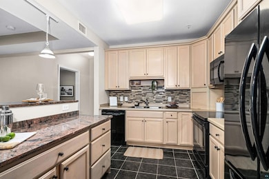 Kitchen with black appliances, decorative backsplash, dark tile patterned flooring, hanging light fixtures, and cream cabinets