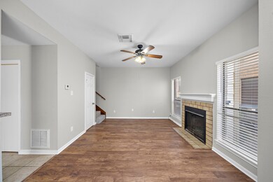 This inviting living room features wood flooring, a cozy fireplace, and ample natural light from large windows. 