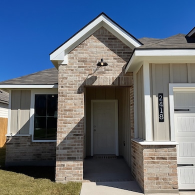 View of exterior entry with a shingled roof and brick siding