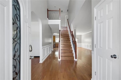 Foyer entrance with arched walkways, dark wood-style flooring, a decorative wall, a wainscoted wall, and stairway