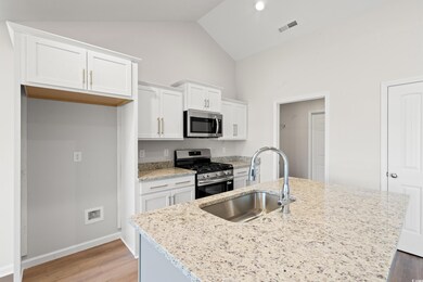 Kitchen with stainless steel appliances, white cabinets, light wood-type flooring, light stone countertops, and high vaulted ceiling