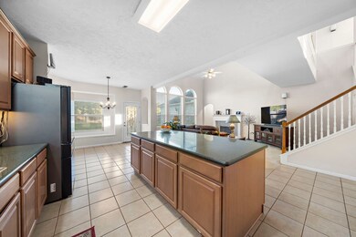 Kitchen with central island, tiled floors, and ample natural light, overlooking a living area with staircase. Fridge not included.