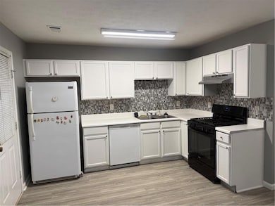 Kitchen with white stove, refrigerator, light countertops, dishwashing machine, and backsplash