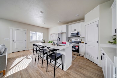 Kitchen with a kitchen bar, a kitchen island with sink, stainless steel appliances, white cabinetry, and light wood-type flooring