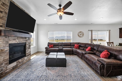Living area with a stone fireplace, wood finished floors, a ceiling fan, recessed lighting, and a textured ceiling