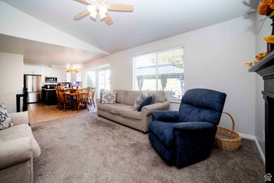 Living room with light colored carpet, lofted ceiling, ceiling fan, a chandelier, and a fireplace
